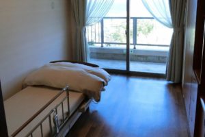 一人部屋の居室です。大きな窓が配置されていてベッドも設置されて、快適に過ごす事が出来ます。（スカイテラス伊東）